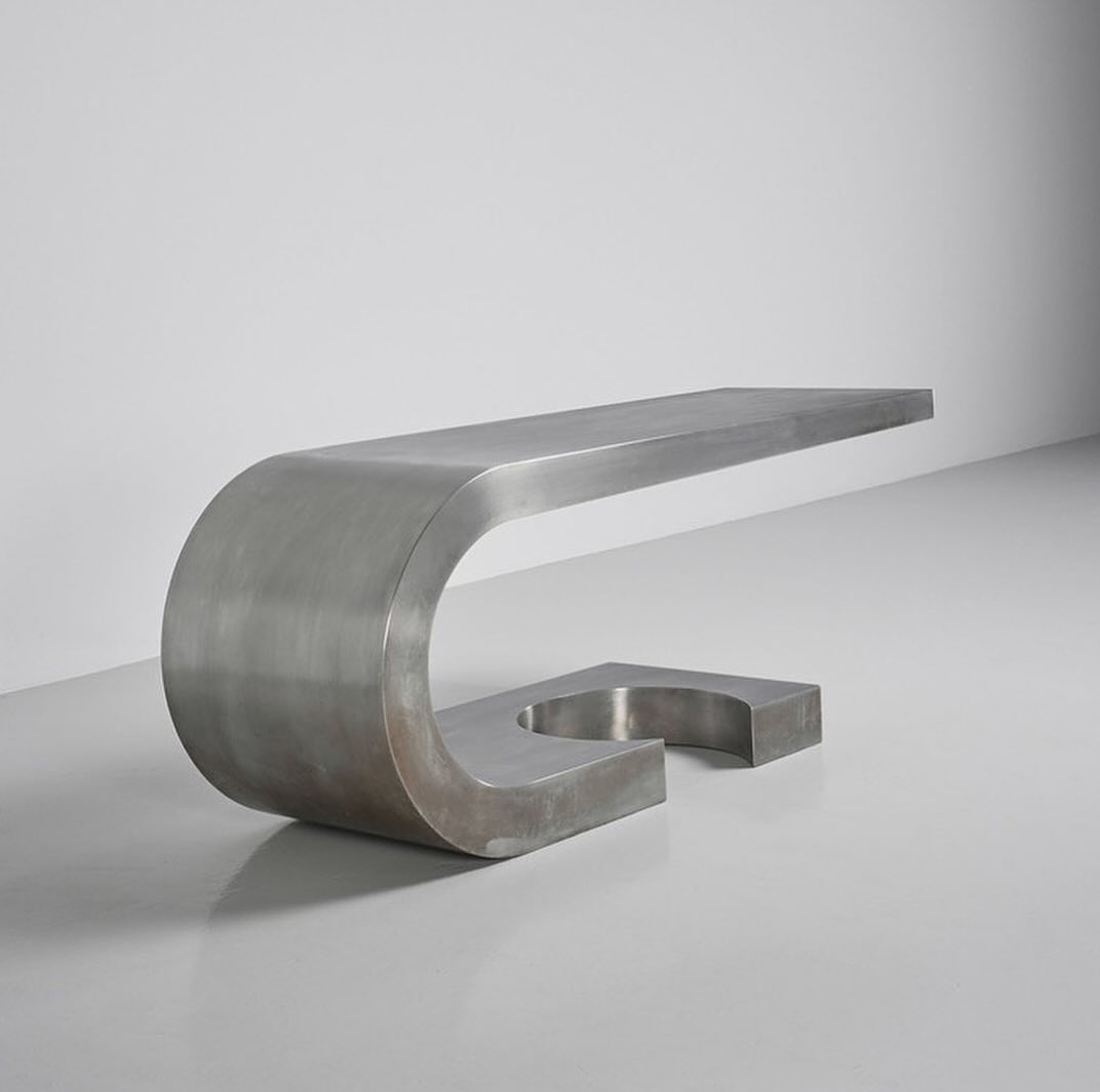 A modern minimalist stainless steel bench with a curved design