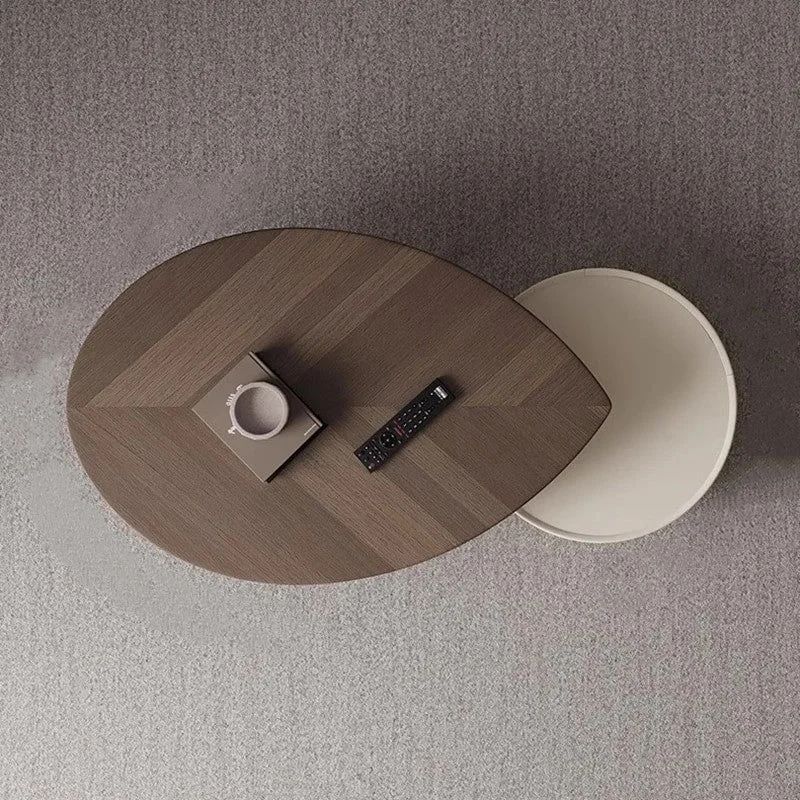 A modern coffee table with a unique two-tier design featuring a dark wood top and a contrasting smaller off-white circular shelf, neatly hosting a remote control, a cup within a square tray.