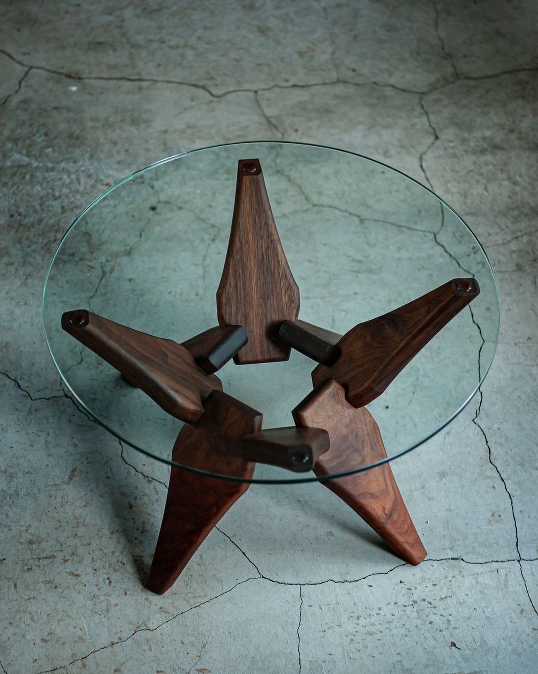 A unique glass top coffee table with a star-shaped wooden base