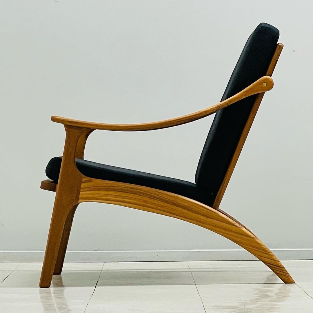 A modern wooden armchair with sleek curves and black cushions