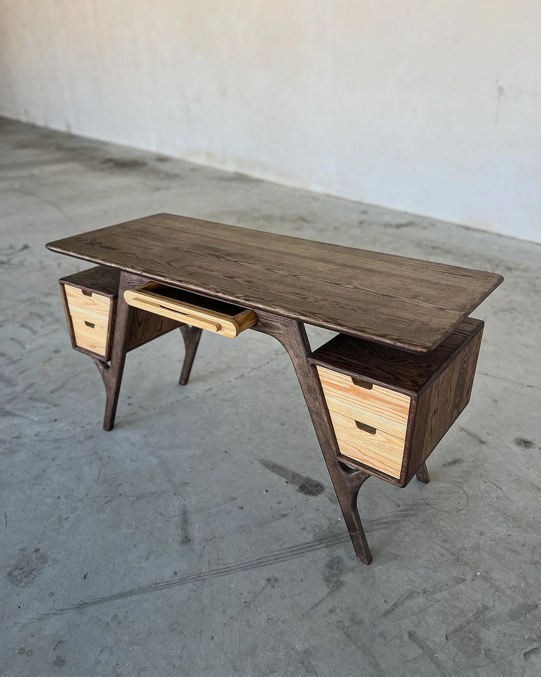 A modern wooden desk featuring unique curved legs and contrasting drawer panels