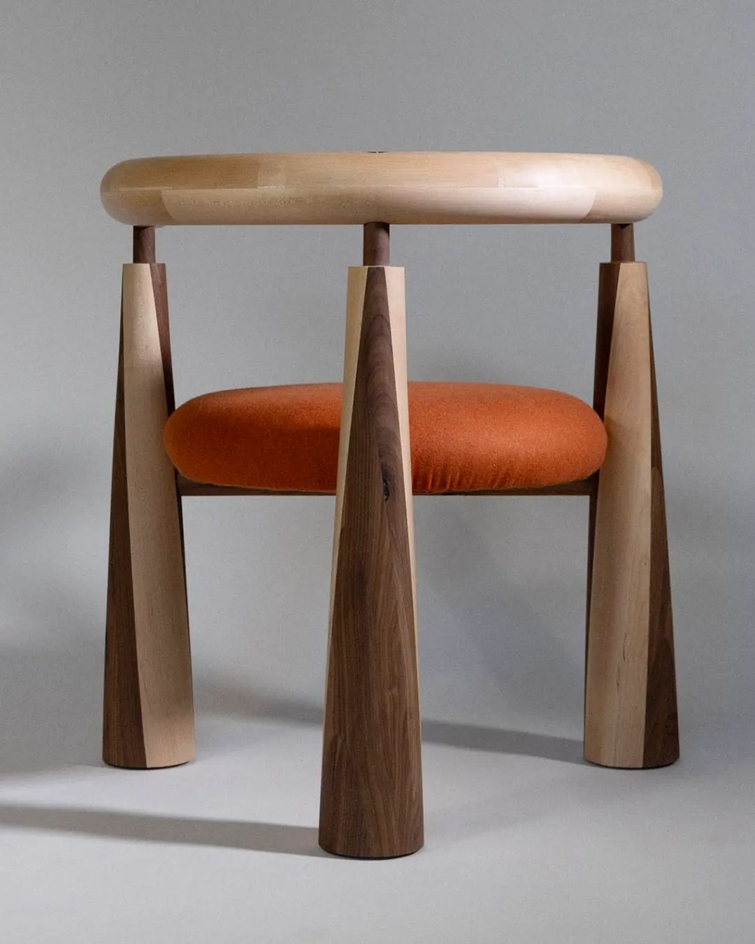 A modern wooden stool with tapered legs and an upholstered burnt orange seat cushion