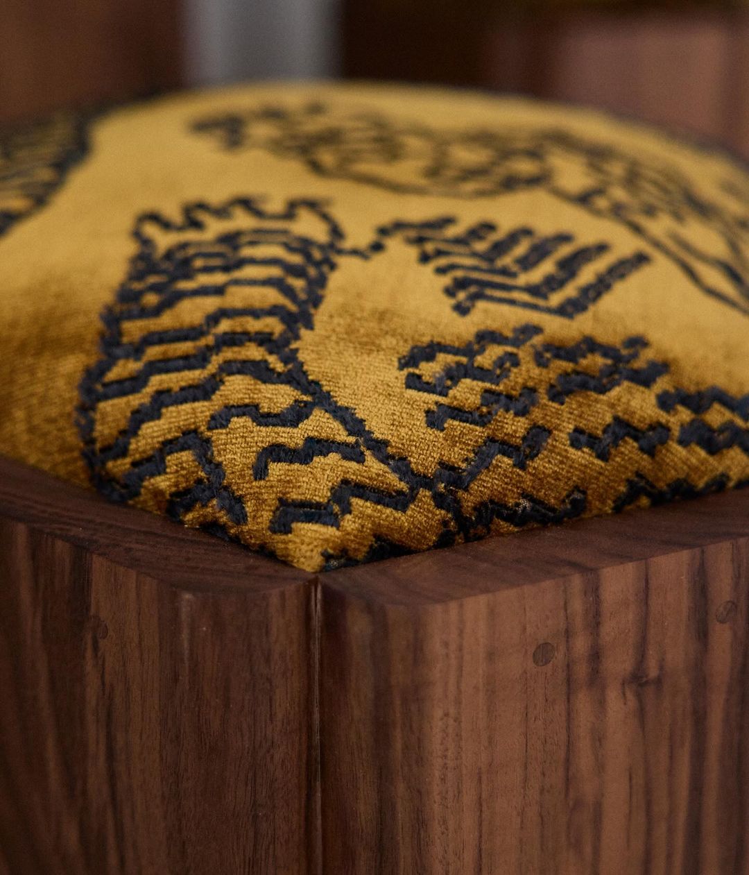 An intricately patterned mustard and navy cushion perched atop a rich wooden base