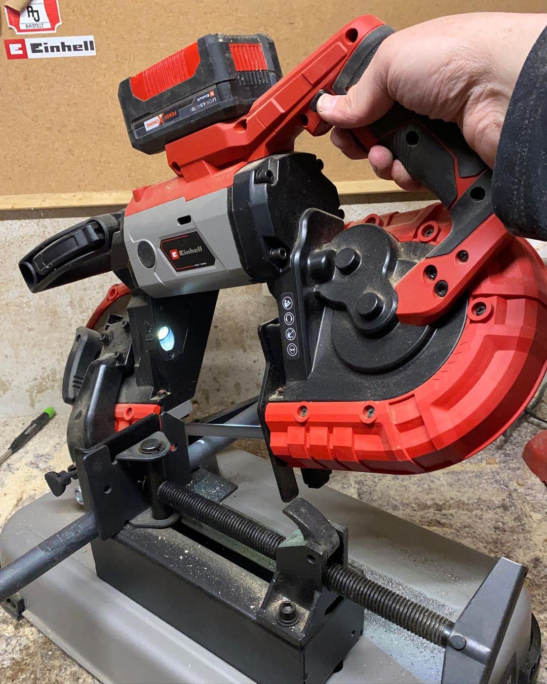 A robust red and black compound miter saw with a human hand adjusting its settings