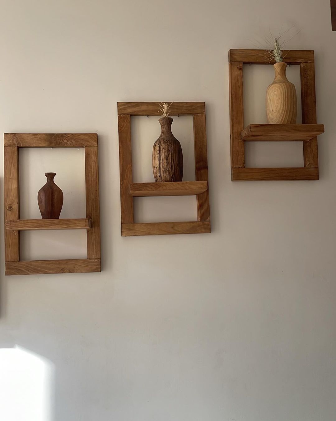 A trio of wooden wall-mounted shelves with rustic ceramic vases, each vase displaying a minimal and naturalistic design.