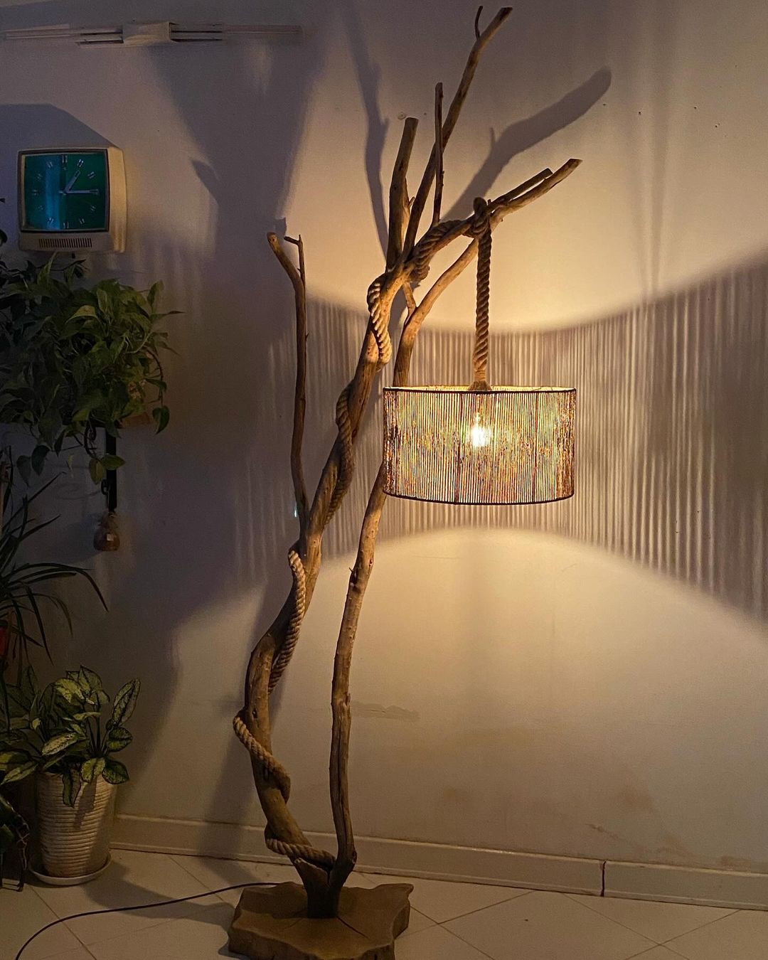 A rustic floor lamp crafted from twisted branches with a rope-suspended drum shade casting a warm glow.