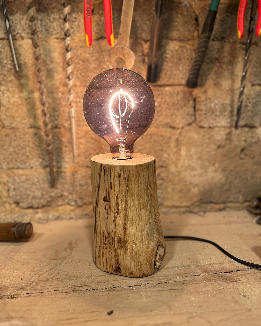 A rustic wooden table lamp with an illuminated vintage-style bulb casting a warm glow