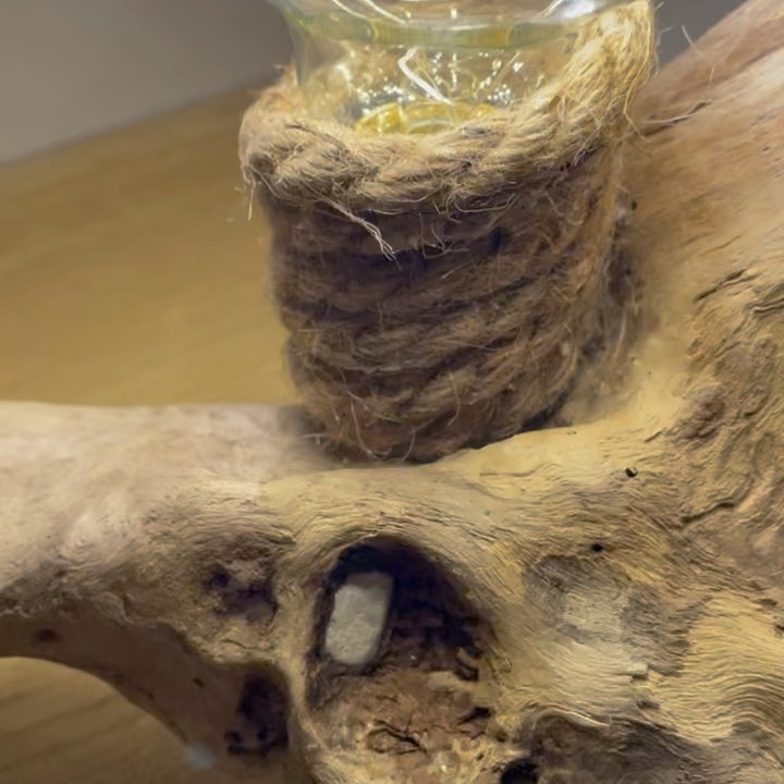 A rustic styled candle holder with twine wrapped around the top section, resting on a textured wooden surface