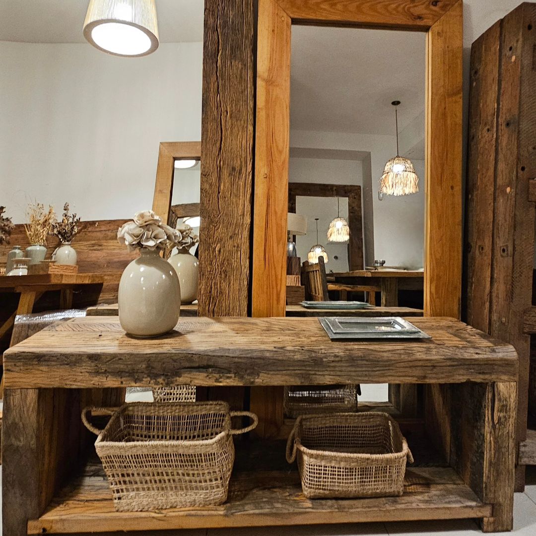 A rustic wooden console table with beige ceramic vases and dried flower arrangements, creating a warm, inviting atmosphere in a room with wooden accents and wicker baskets beneath.