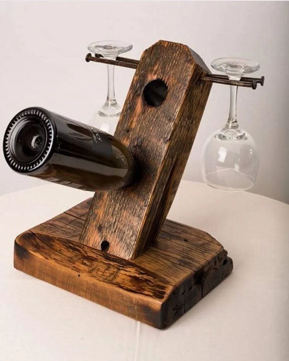 A rustic-style wine bottle and glass holder crafted from reclaimed wood, featuring a horizontal rod for hanging two wine glasses and a carved out space for securing the wine bottle in place.