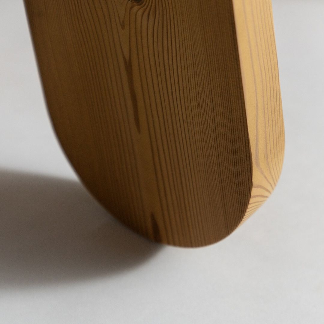 A minimalist wooden object showing a smooth, curved shape with pronounced wood grain