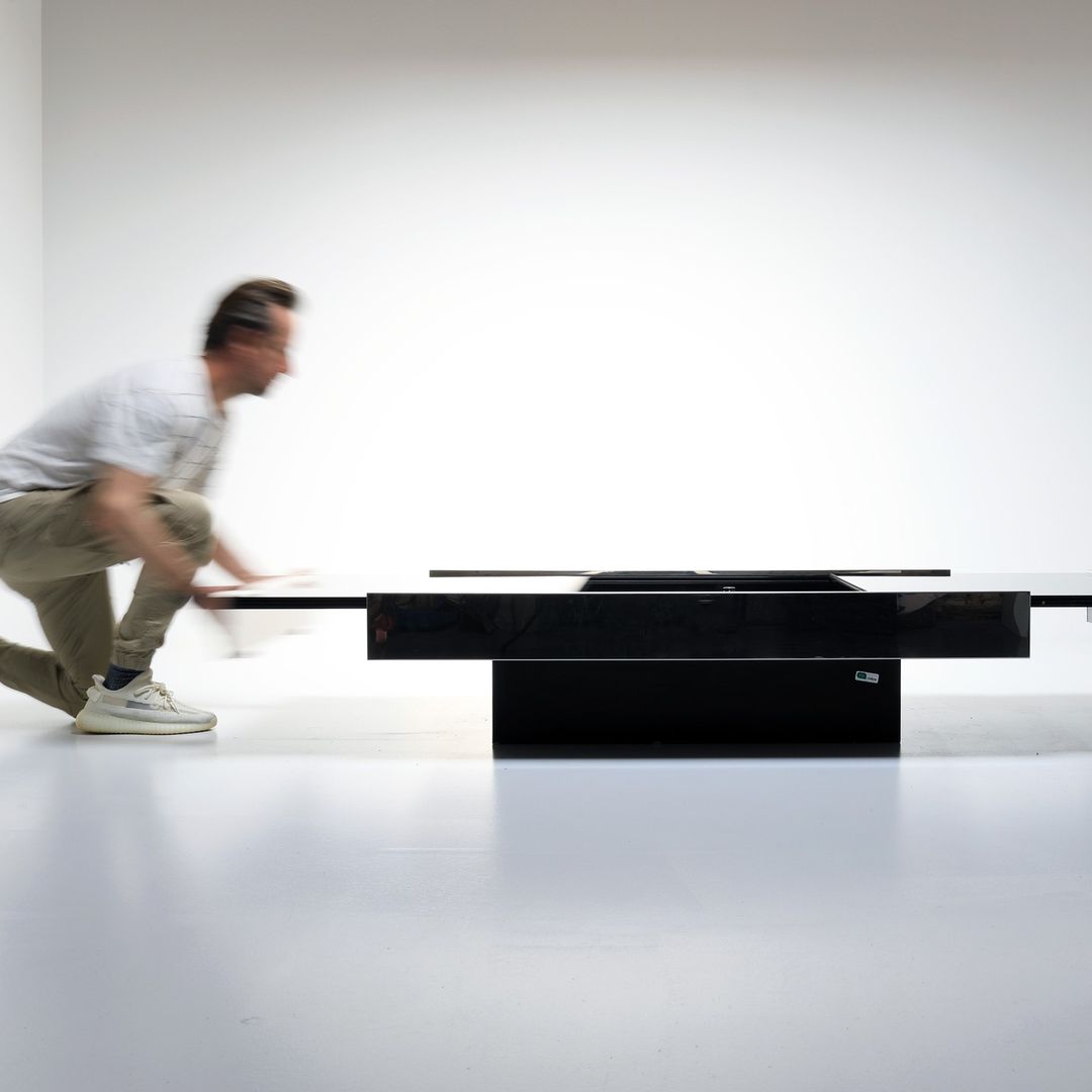 An individual seemingly in motion in a minimalistic room with a modern black piece of furniture