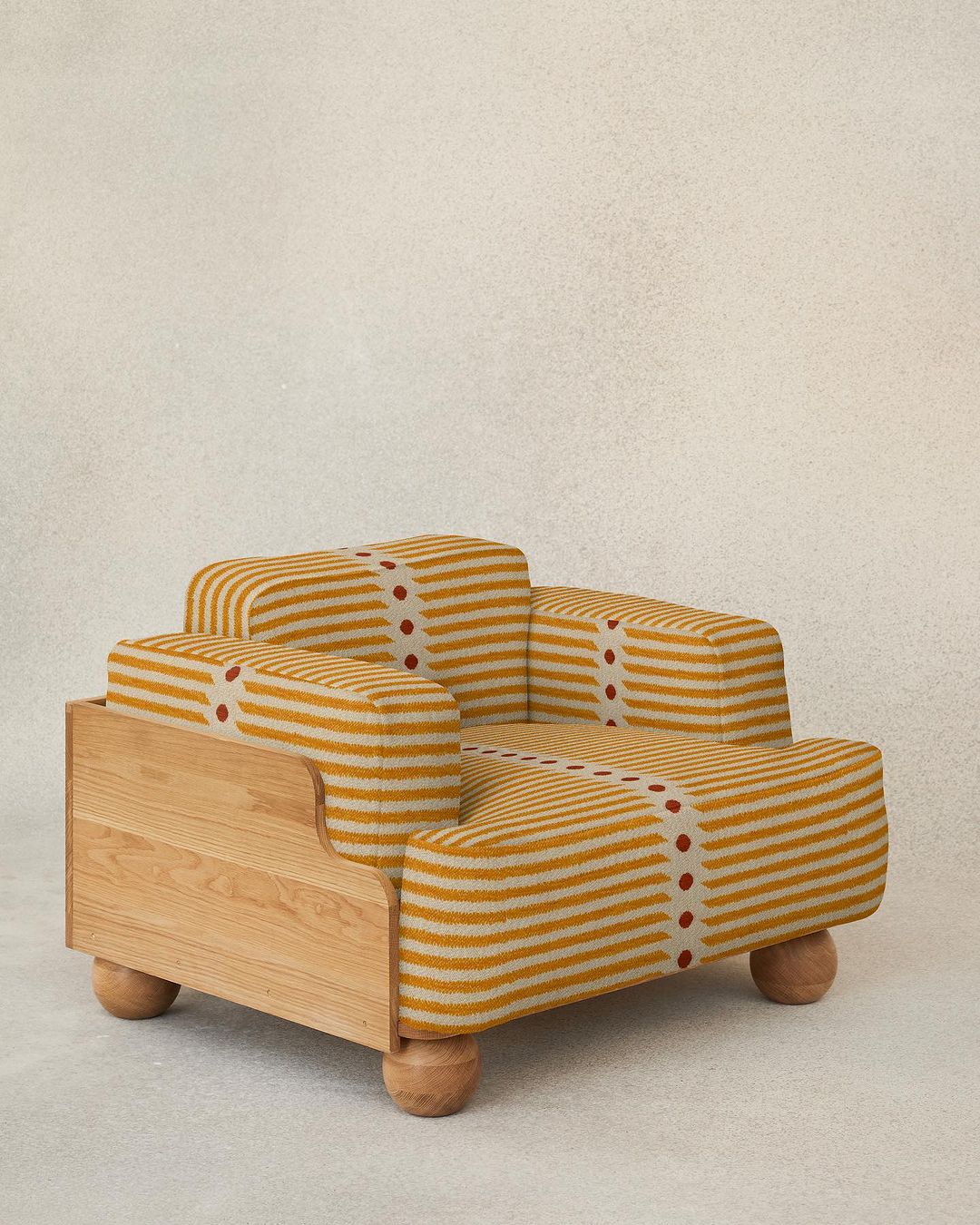 A uniquely designed armchair with a stripy yellow and white upholstery and rounded wooden feet