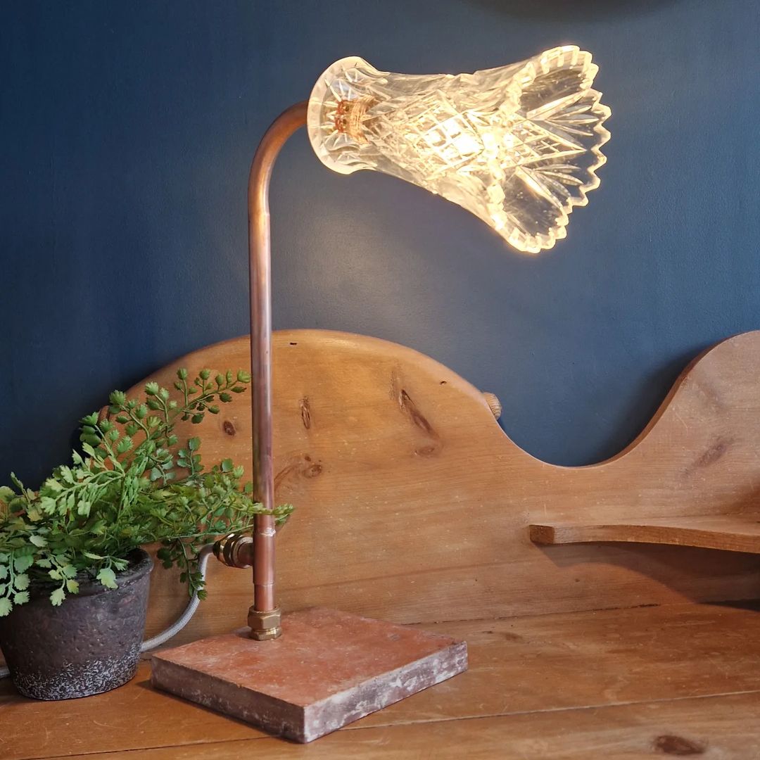 A unique and stylish desk lamp with a copper stand and an intricately patterned glass shade