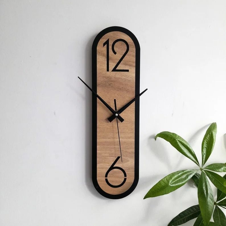 Modern wooden wall clock on a white background with a green plant leaf to the side