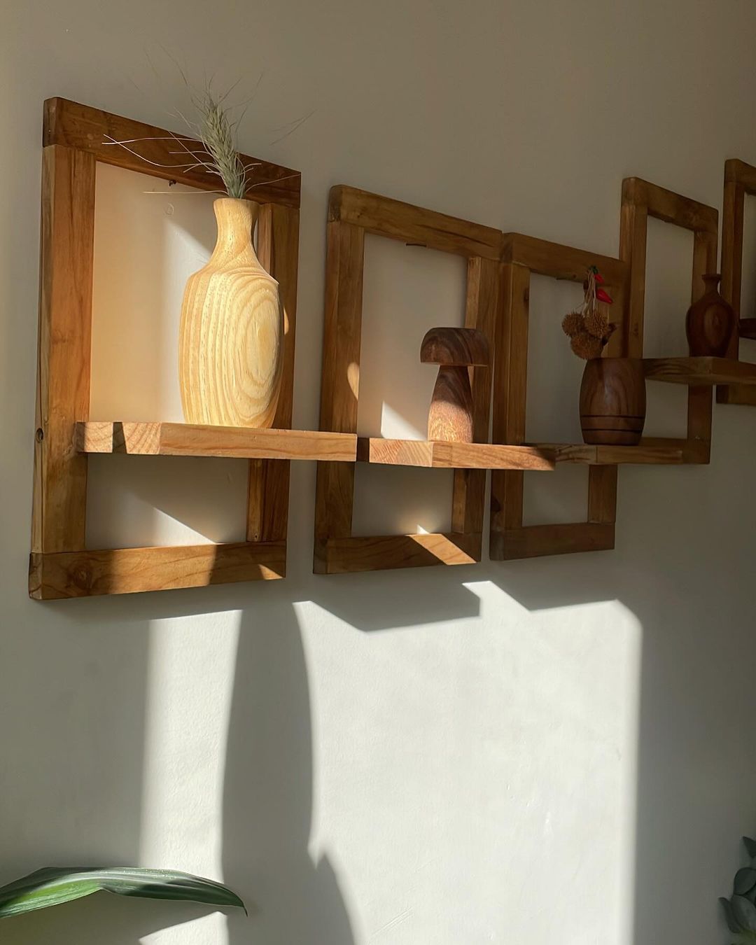 A warm sunlight illuminates wooden wall shelves featuring an array of decorative vases and wooden ornaments.