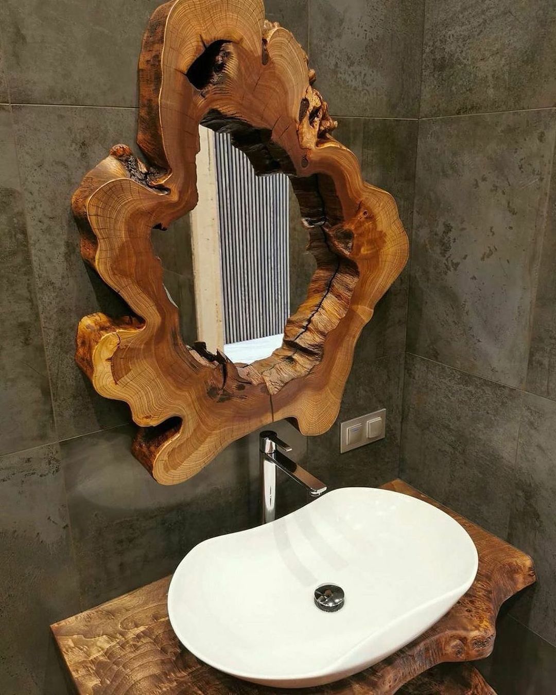 A uniquely crafted bathroom with a rustic wooden mirror frame over a modern white oval sink