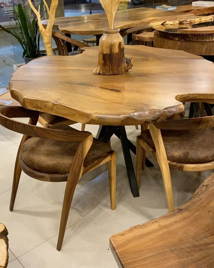 A uniquely shaped wooden dining table with natural edges and a central stump base surrounded by matching wooden chairs with suede upholstery.