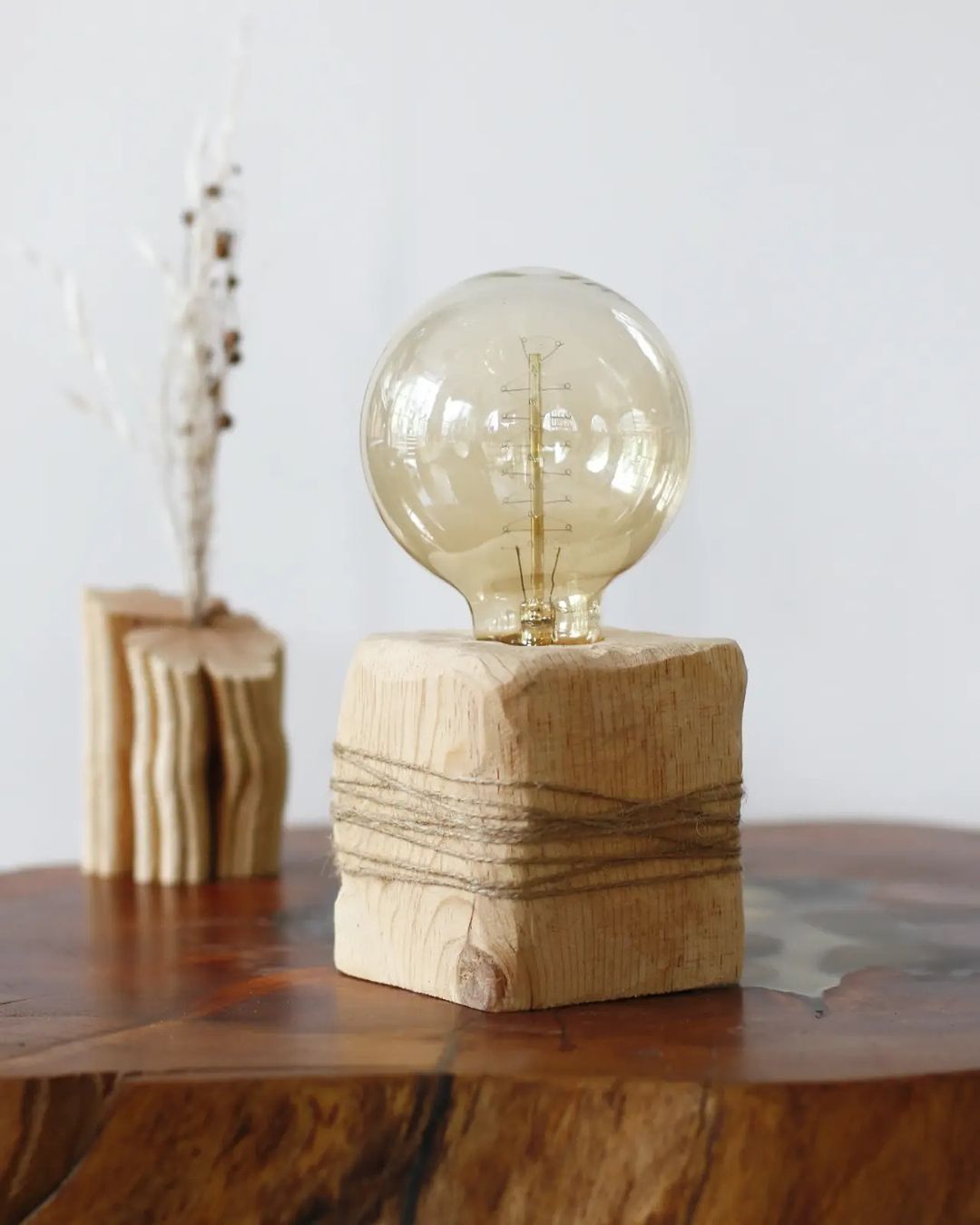 A wooden base supporting a spherical clear light bulb