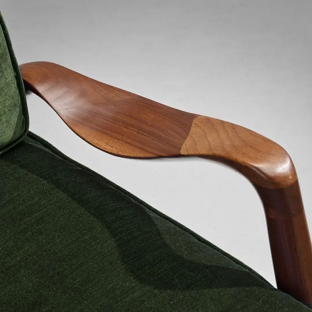 A vintage chair with a sleek wooden armrest and plush green upholstery