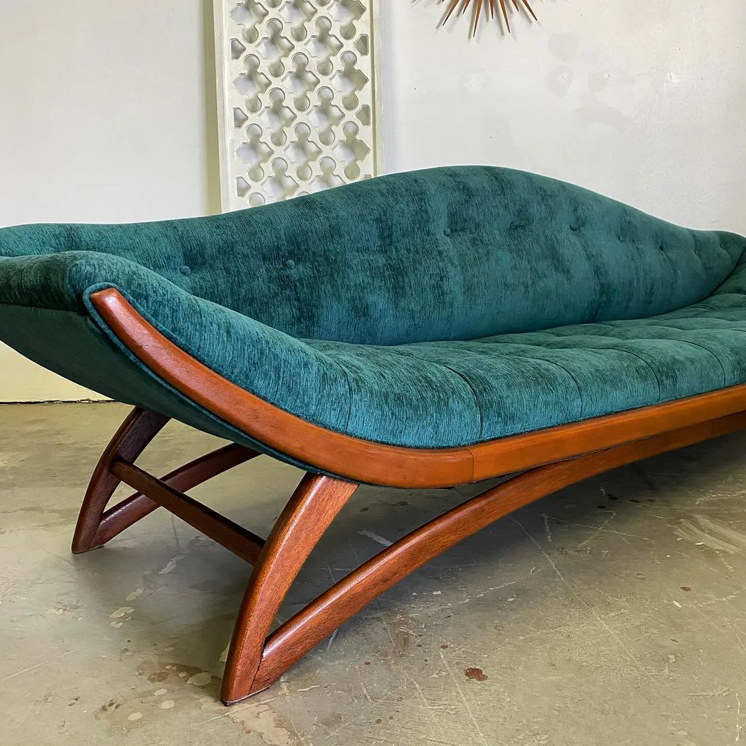 A vintage teal velvet sofa with a curvaceous silhouette and solid wood legs