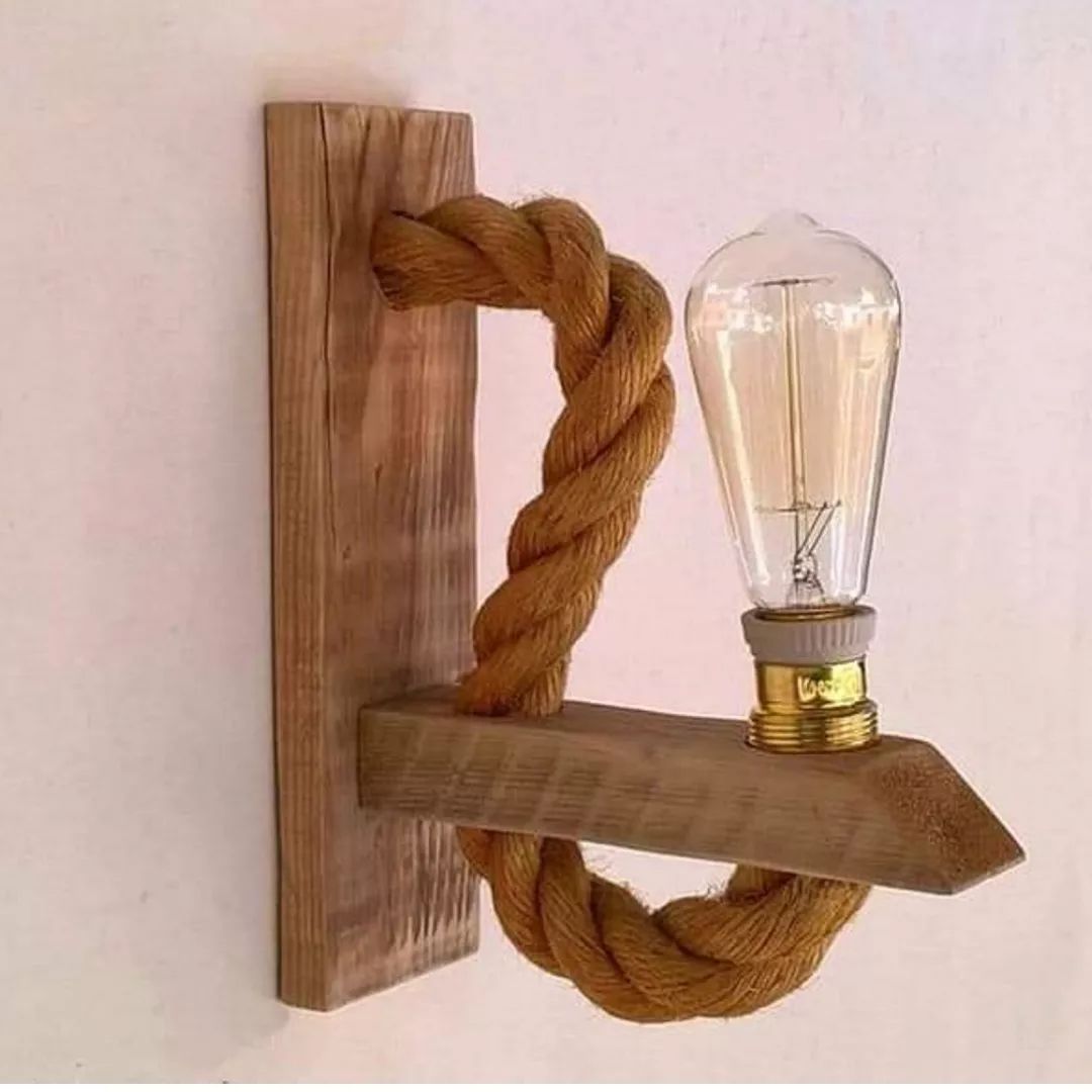 A unique wall-mounted lighting fixture with an industrial design featuring a thick twisted rope as a support structure and an Edison bulb for a vintage touch.