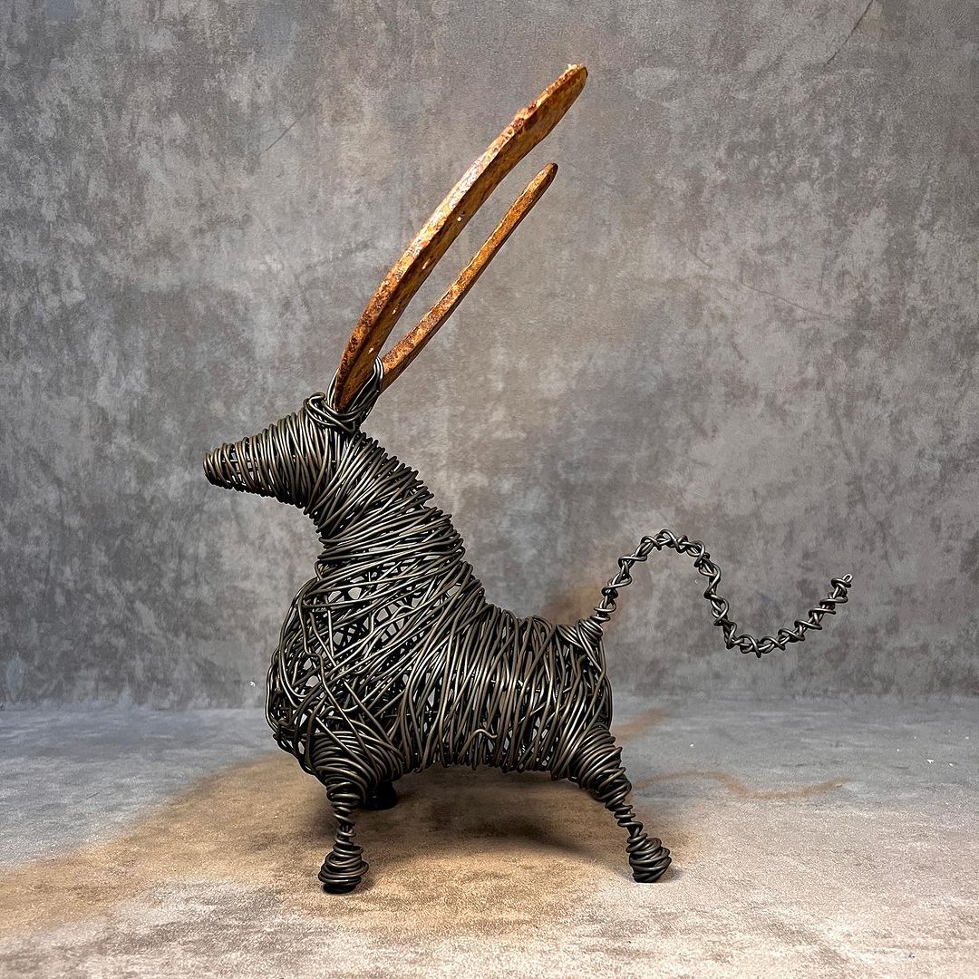 A whimsical wire sculpture of a rabbit with elongated, rusty metal ears