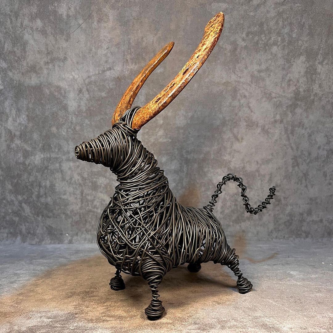 A whimsical wire sculpture of an imaginary creature with elongated, rust-toned ears and a spiraled tail