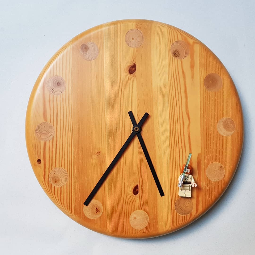 A wooden wall clock with a unique twist: one of the hour markers is represented by a miniature figurine climbing up the side.